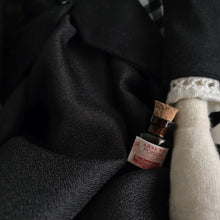 Load image into Gallery viewer, We see a wee bottle of Arsenic resting beside Madeleine's hand