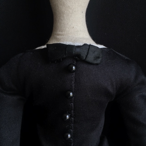 A close up of Madeleine's body from her neck to mid torso, set against a dark back drop. The focus is on the row of buttons on her jacket, the antique silk bow at her neckline, and a peek of the antique linen at her collar.